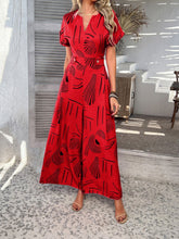 Lifestyle shot of scarlet Serenoor jumpsuit styled with tan heels and woven clutch on a resort vacation.