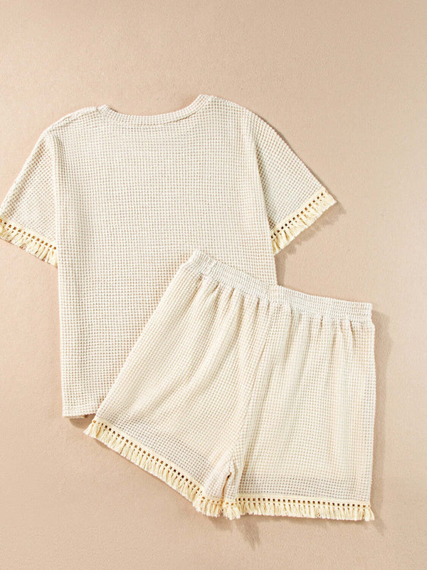 Flatlay back view of the cream Shakaluxe set with tassel details tassel with a dark tan background.
