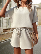 Model wearing the beige Soft But Savage Shorts Set paired with a light brown straw hat, sunglasses, jewelry, and a light brown straw handbag for city stroll.