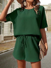 a model wearing the green Soft But Savage Half Sleeve Shorts Set paired with a light brown straw hat, sunglasses, jewelry, and a light brown straw handbag.