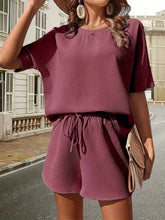 a model wearing the moonlit mauve Soft But Savage Shorts Set paired with a light brown straw hat, sunglasses, jewelry, and a light brown straw handbag.