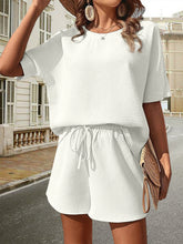 a model wearing the white Coral Cove Half Sleeve Shorts Set paired with a light brown straw hat, sunglasses, jewelry, and a light brown straw handbag