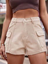 Woman in a linen button-down shirt and tan Joyful Journey Denim shorts browsing in a vintage market.