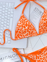 Close-up flat lay detail of hot tangerine leopard print tie side bikini set showing halter neck and side tie string details