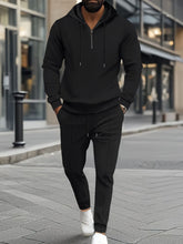 A man shopping in New York City wearing the Tavvion TerrainFlex  Waffle-Knit Half Zipper Hoodie and Pants Set in black paired with white sneakers.