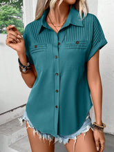 Model wearing a teal pleated collared neck short sleeve blouse with button-up front, paired with light denim jeans, styled for a casual day out.