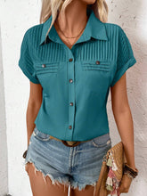 Side profile of model in a teal pleated collared neck blouse with cuffed sleeves, styled with gold hoop earrings and neutral sandals.