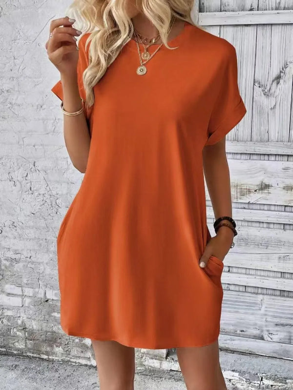 Model posing in Terracotta Rahluna Mini Tee Dress at a weekend brunch styled with gold hoop earrings, sneakers, and a crossbody bag.