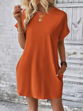 Model posing in Terracotta Rahluna Mini Tee Dress at a weekend brunch styled with gold hoop earrings, sneakers, and a crossbody bag.