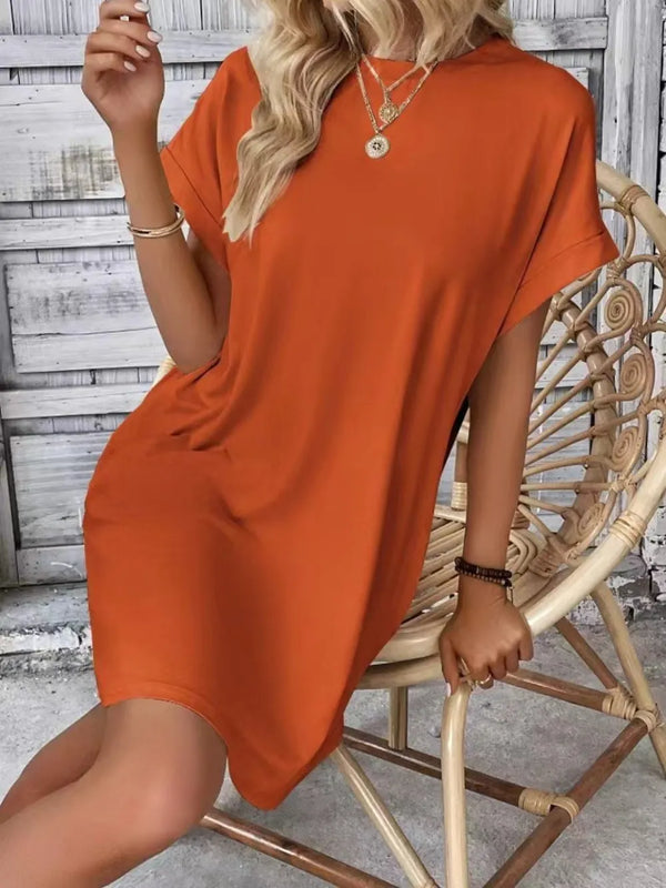 Woman seated outdoors in Terracotta Rahluna Mini Tee Dress paired with ankle boots and a denim jacket draped over her shoulders.