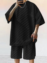 Front view of man taking a selfie photo wearing black Therion Boldline Set with round neck checkered shirt and shorts, styled with sneakers and accessories.