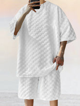 Front view of man taking a selfie photo wearing white Therion Boldline Set with round neck checkered shirt and shorts, styled with sneakers and accessories.