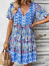 Model wearing Vesaluna Paisley Print Tie Neck Dress in blue, styled with a straw hat and nude heels for a chic daytime look.