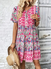 Model wearing Vesaluna Paisley Print Tie Neck Dress in pink at an outdoor garden party with a vintage clutch and sandals.