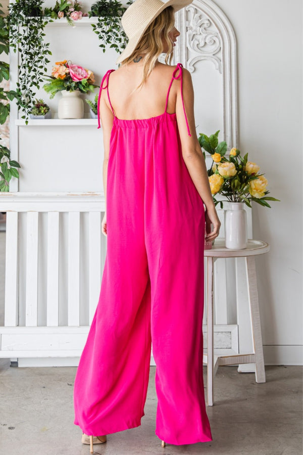 Back view of the model in a Fuchsia Veveret Pocketed Spaghetti Strap Wide Leg Jumpsuit paired with a straw hat and tan heels.