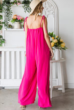 Back view of the model in a Fuchsia Veveret Pocketed Spaghetti Strap Wide Leg Jumpsuit paired with a straw hat and tan heels.