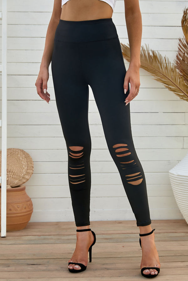 Model in front view wearing black distressed leggings with heels, showcasing slim fit and edgy rip details.