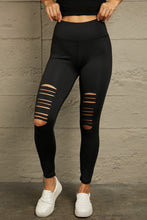 Model in front view wearing distressed black leggings with sneakers, styled for casual streetwear look.
