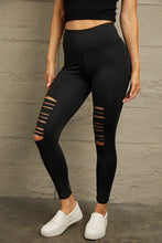Left side angle view of model in black distressed leggings, featuring ripped detailing and sleek fabric texture.