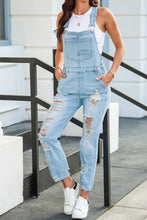 Model showcases Vixéa’s distressed light blue denim, square neckline, and adjustable buckle straps, sitting on a rail in front of an urban city building.