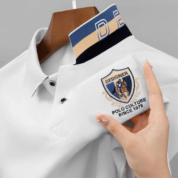 Close-up front view of white Equestrian Crest Designer Polo on hanger showing embroidery, buttons, and flip color-contrast collar.