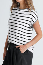 Woman wearing white striped knit short sleeve top at a weekend market, styled with shorts, sneakers, and a crossbody bag.