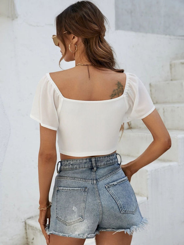 Back view of Glowflutter Crop Top showing soft fabric and flutter sleeve flow, worn by model in white.