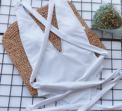  Close-up flat lay detail of white halter neck deep V tied one-piece swimsuit showing fabric texture and adjustable straps