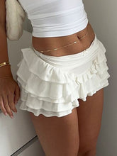 White Rivéla Ruche Skirt front angle pose with mini bow accent, styled with crop top, gold bracelets, plush white shoulder pure, and gold belly chain