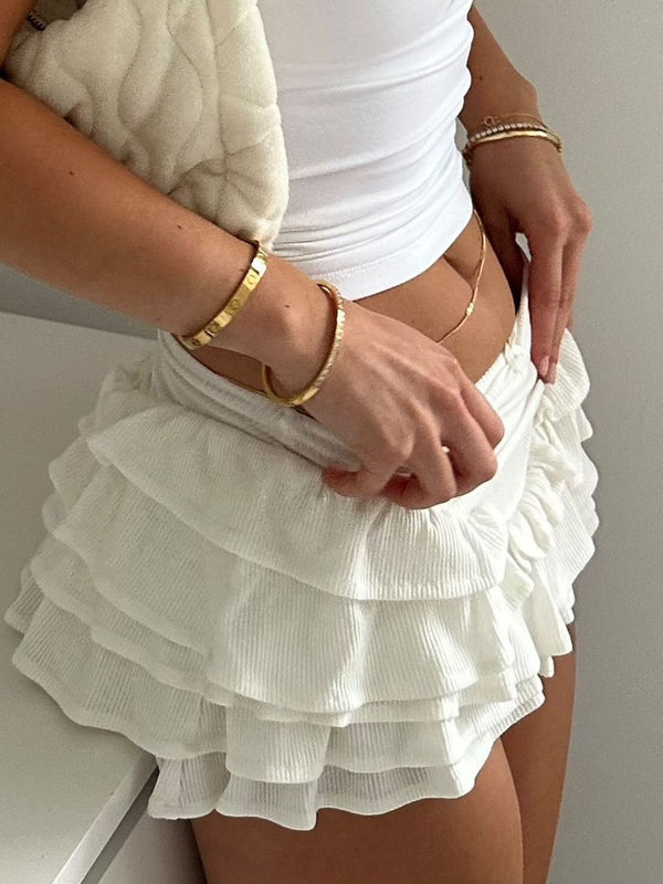 Model styling White Rivéla Ruche Skirt with crop top, purse, and gold accessories