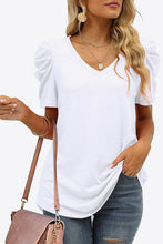 Female model wearing a white V-neck puff sleeve tee with soft stretch fabric and gathered sleeves, styled with denim jeans.