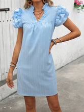 Woman wearing the pastel blue ruffled notched cap sleeve mini dress with one hand on her hip.