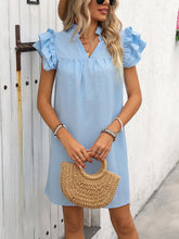 Woman wearing the Pastel Blue ruffled notched cap sleeve mini dress with a straw handbag poolside.
