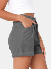 Close up photo of woman highlighting the pocket detailing of the Dark Gray Metropolitan Maven High-Waist Shorts paired with a white tank top and jewelry. 