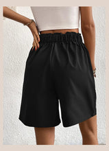 Women's black partial elastic high waist pleated baggy trouser shorts, back view.