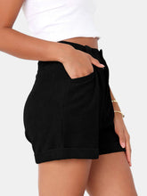 Close up photo of female model highlighting the pocket detailing of the Black Metropolitan Maven High-Waist Shorts from the side paired with a white tank top and jewelry. 
