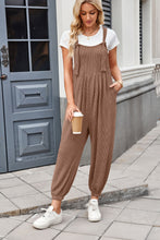 Model styling brown Xévia Overalls with a tank top, gold hoop earrings, and classic white sneakers for a relaxed daytime look.
