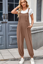 Model styling brown Xévia Overalls with a tank top, gold hoop earrings, and classic white sneakers for a relaxed daytime look.