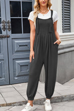 Model styling dark gray Xévia Overalls with minimalist jewelry, a crossbody bag, and sneakers for a casual streetwear look.