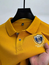 Close-up front view of yellow Equestrian Crest Designer Polo on hanger showing embroidery, buttons, and flip color-contrast collar.