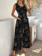 Model accessorized with gold jewelry and heels, wearing black Zauraphina jumpsuit.
