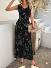 Model wearing black Zauraphina jumpsuit with elegant all-over print, standing in a vacation rental beachhouse.